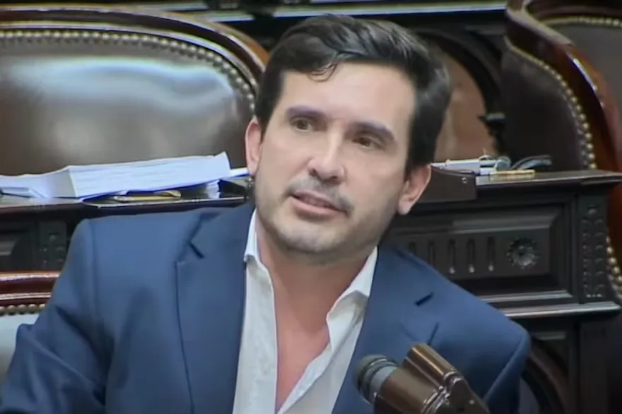 Un hombre de traje habla ante un micrófono en un recinto legislativo