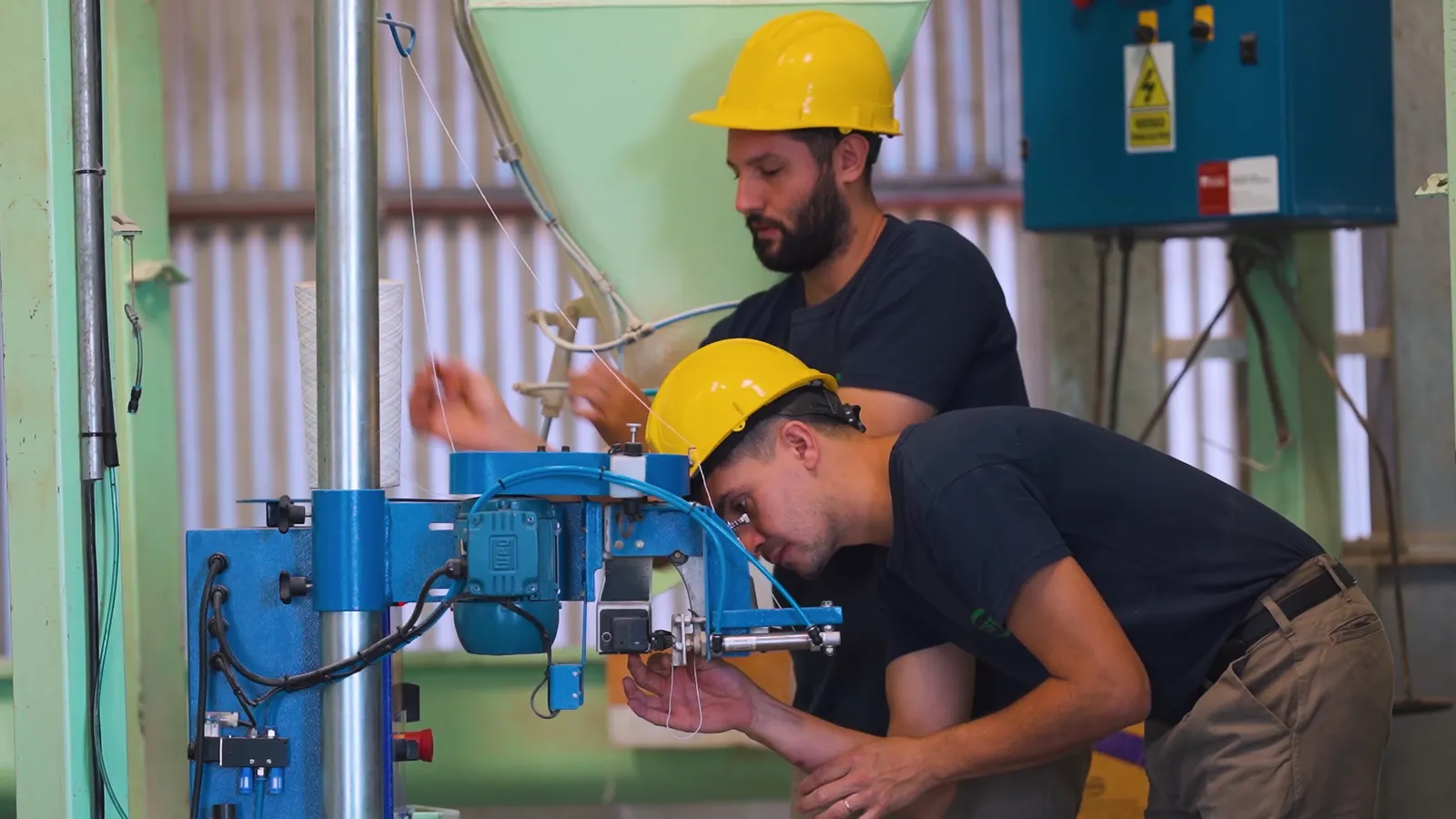 Dos operarios con casco trabajan en una máquina dentro de una planta industrial